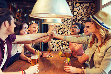 Image showing happy friends with drinks making high five at bar