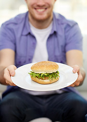 Image showing close up of man holding hamburger on plate at home