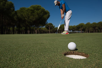 Image showing golf player hitting shot, ball on edge of hole