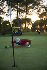 Image showing golf player blowing ball in hole with sunset in background