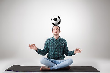 Image showing Portrait  of young man, practicing yoga with football ball