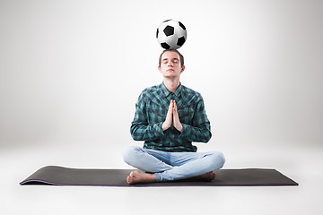 Image showing Portrait  of young man, practicing yoga with football ball