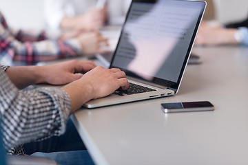 Image showing close up of business man hands typing on laptop with team on mee