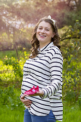 Image showing pregnant woman holding baby shoes in her hands in a park