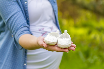 Image showing close up of pregnant woman hand with baby shoes 