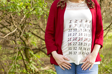 Image showing Pregnant woman in red jacket with calendar on her T-shirt outdoo