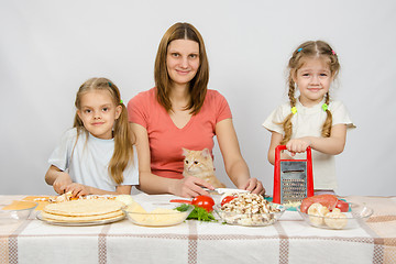Image showing Mother and two little girls at a table prepared ingredients for the pizza. They were watching a cat