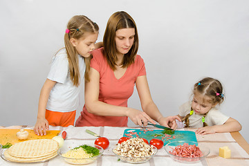 Image showing Two daughters are watching with interest as the mother chopped green