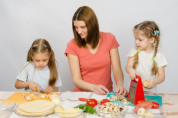 Image showing Mum with a five-year daughter watched as the eldest daughter cutting mushrooms pizza