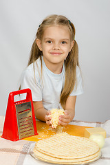 Image showing The little girl at the table rubbed grated cheese for pizza