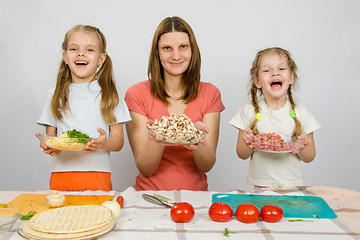 Image showing Mother with two daughters happily holding a plate with sliced products for pizza