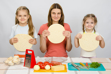 Image showing Mum with two little girls sitting in a row at the kitchen table and a hand-held pizza bases