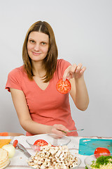 Image showing The girl at the kitchen table holding two fingers chopped tomato circle