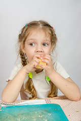 Image showing Six-year girl with pigtails trying to bite off a piece of cheese that keeps both hands