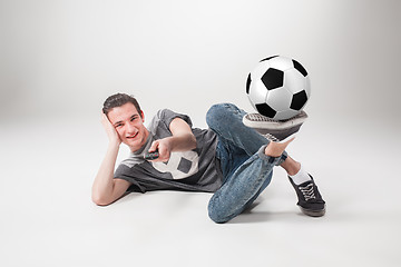 Image showing The portrait of fan with ball, holding  tv remote on gray background