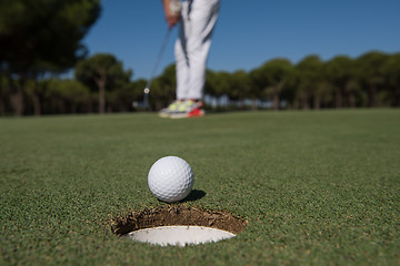 Image showing golf player hitting shot, ball on edge of hole