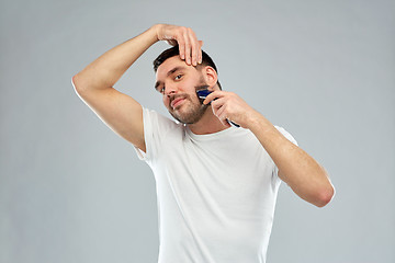 Image showing smiling man shaving beard with trimmer over gray