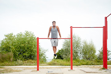 Image showing young man exercising on horizontal bar outdoors