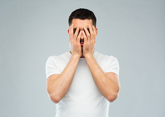 Image showing man in white t-shirt covering his face with hands