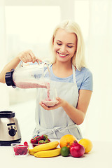 Image showing smiling woman with blender preparing shake at home