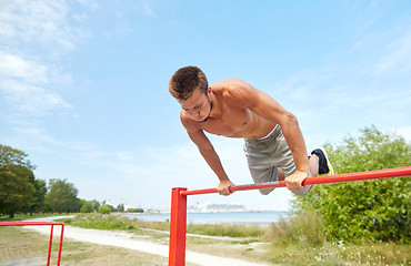 Image showing young man exercising on horizontal bar outdoors