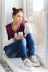 Image showing teenage girl sitting on windowsill with smartphone