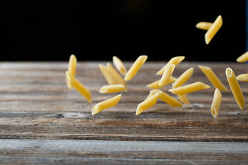 Image showing Falling penne pasta. Flying yellow raw macaroni over black background.