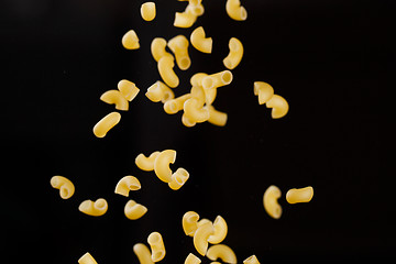 Image showing Falling gobetti pasta. Flying yellow raw macaroni over black background. 
