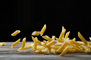 Image showing Falling penne pasta. Flying yellow raw macaroni over black background.