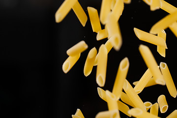 Image showing Falling penne pasta. Flying yellow raw macaroni over black background.