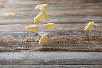 Image showing Falling penne pasta. Flying yellow raw macaroni over black background.