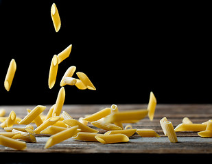 Image showing Falling penne pasta. Flying yellow raw macaroni over black background.