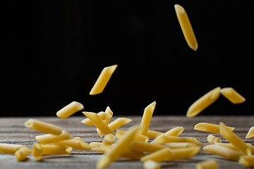 Image showing Falling penne pasta. Flying yellow raw macaroni over black background.