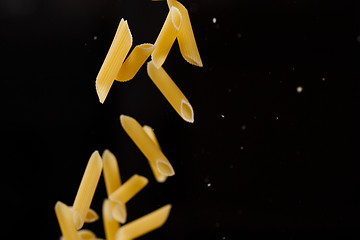 Image showing Falling penne pasta. Flying yellow raw macaroni over black background.