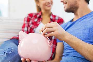 Image showing close up of happy couple putting coin to piggybank