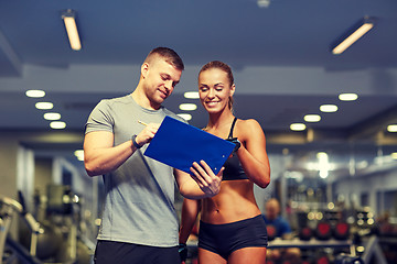 Image showing smiling young woman with personal trainer in gym