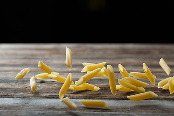 Image showing Falling penne pasta. Flying yellow raw macaroni over black background.