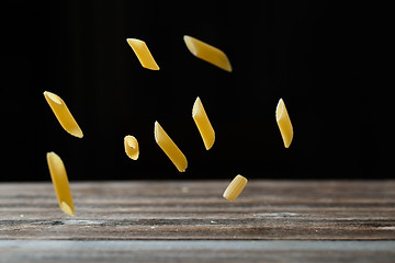 Image showing Falling penne pasta. Flying yellow raw macaroni over black background.