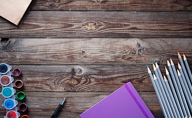 Image showing Watercolors, color pencils and sketchbook on wooden table. Flat lay photo with empty space for logo, text.