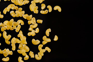 Image showing Falling gobetti pasta. Flying yellow raw macaroni over black background. 