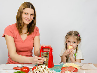 Image showing The girl at the kitchen table t cheese grater sitting next to a five-year daughter and eats cheese