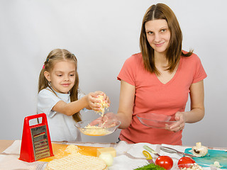 Image showing  Six-year girl helps mother to rub grated cheese on pizza