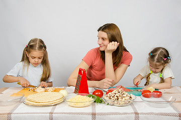 Image showing Satisfied mother watching her little daughter to help her cut products at the kitchen table