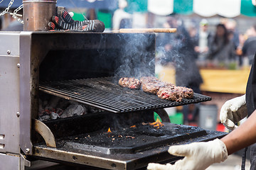 Image showing Beef burgers being grilled on food stall grill.