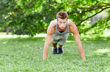 Image showing young man doing push ups on grass in summer park