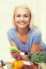 Image showing smiling woman with smartphone cooking vegetables