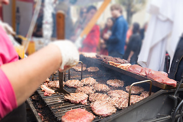 Image showing Beef burgers being grilled on food stall grill.