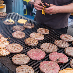 Image showing Beef burgers being grilled on food stall grill.