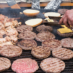 Image showing Beef burgers being grilled on food stall grill.