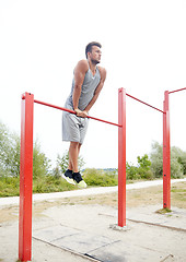 Image showing young man exercising on horizontal bar outdoors